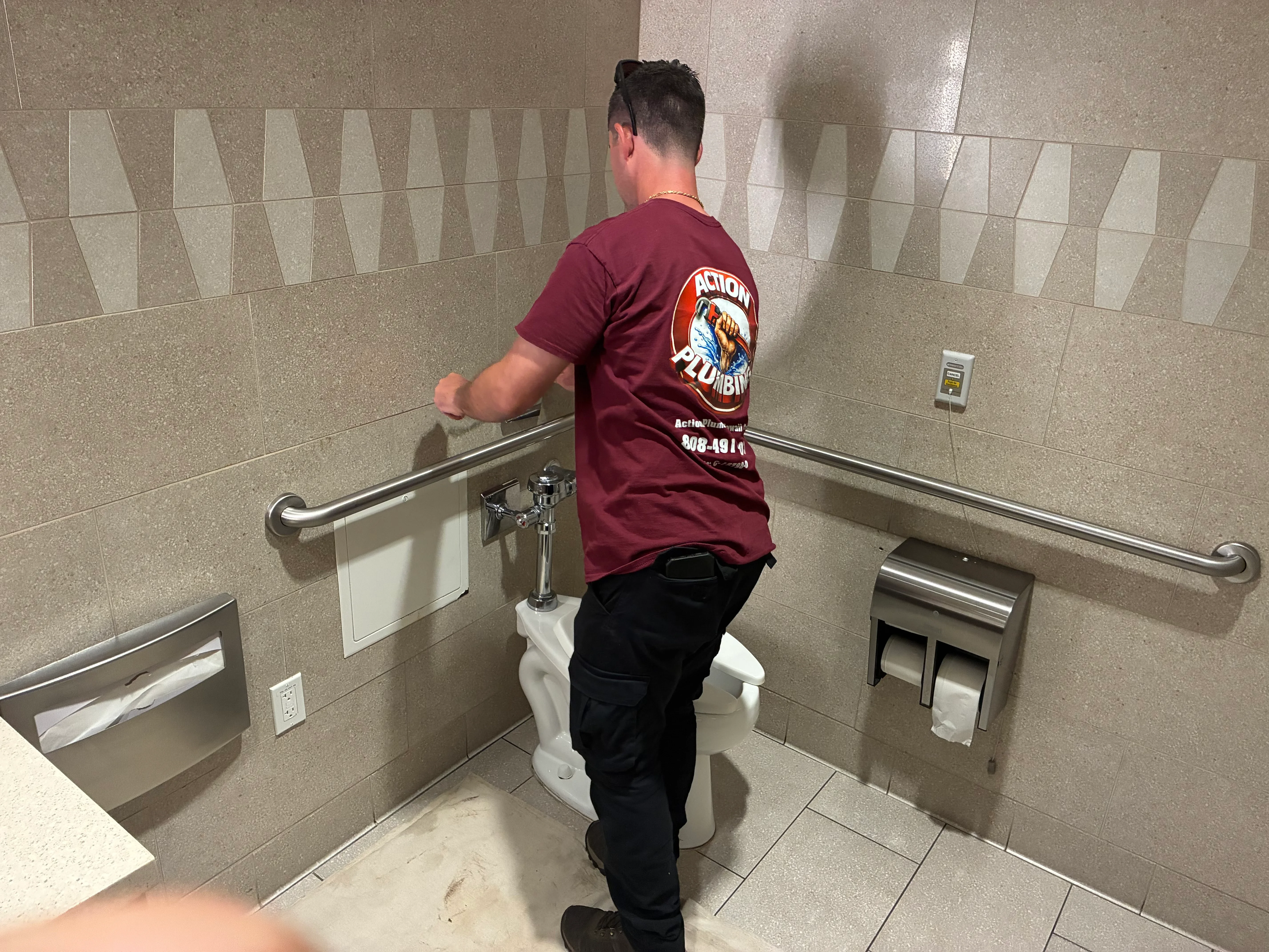 Plumber installing stainless steel grab bars and fixtures in tiled commercial bathroom