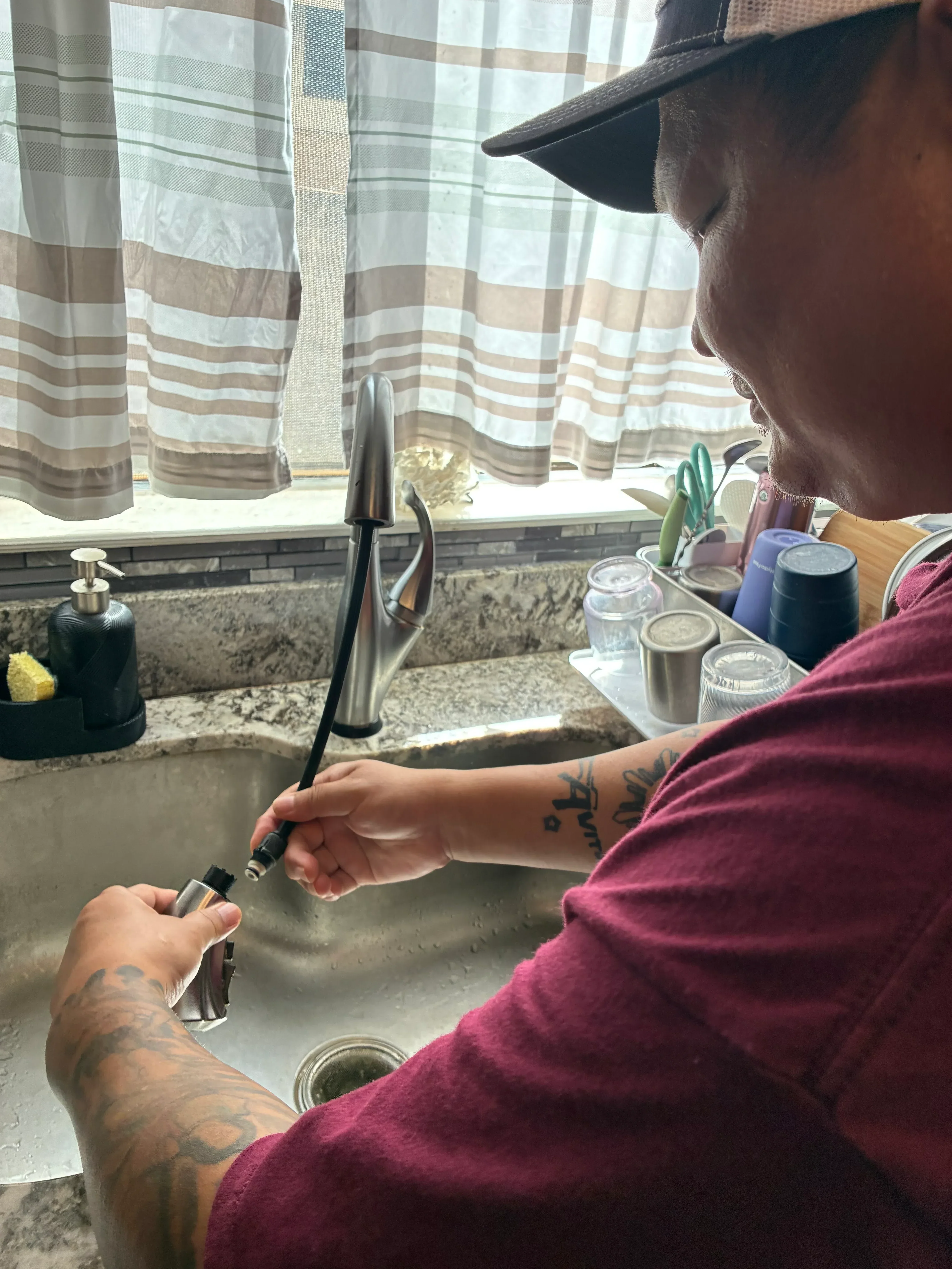 Plumber installing chrome faucet with connection lines and supply lines visible under sink