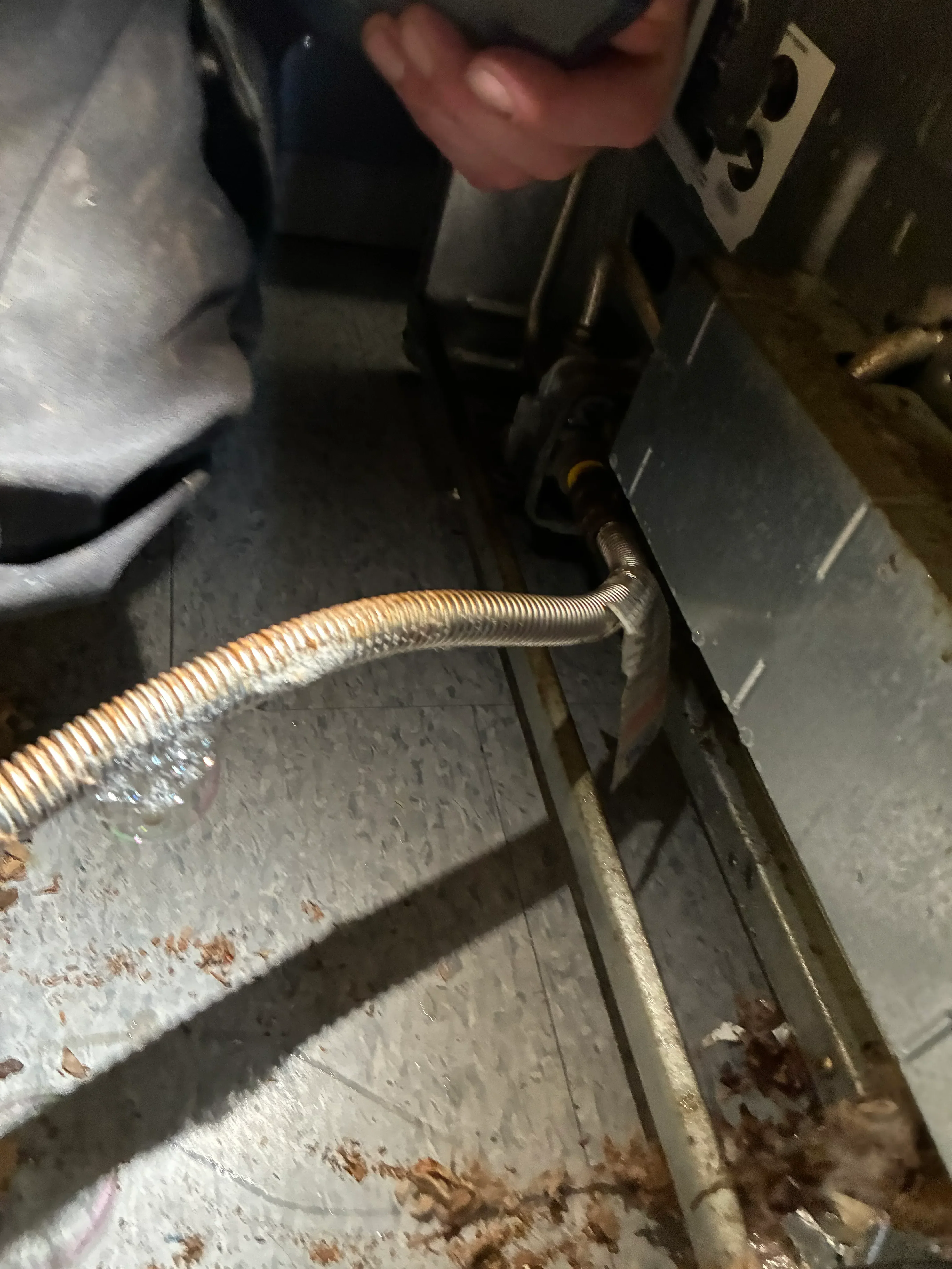 Corrugated stainless steel gas line connected to black fitting with secure mounting brackets