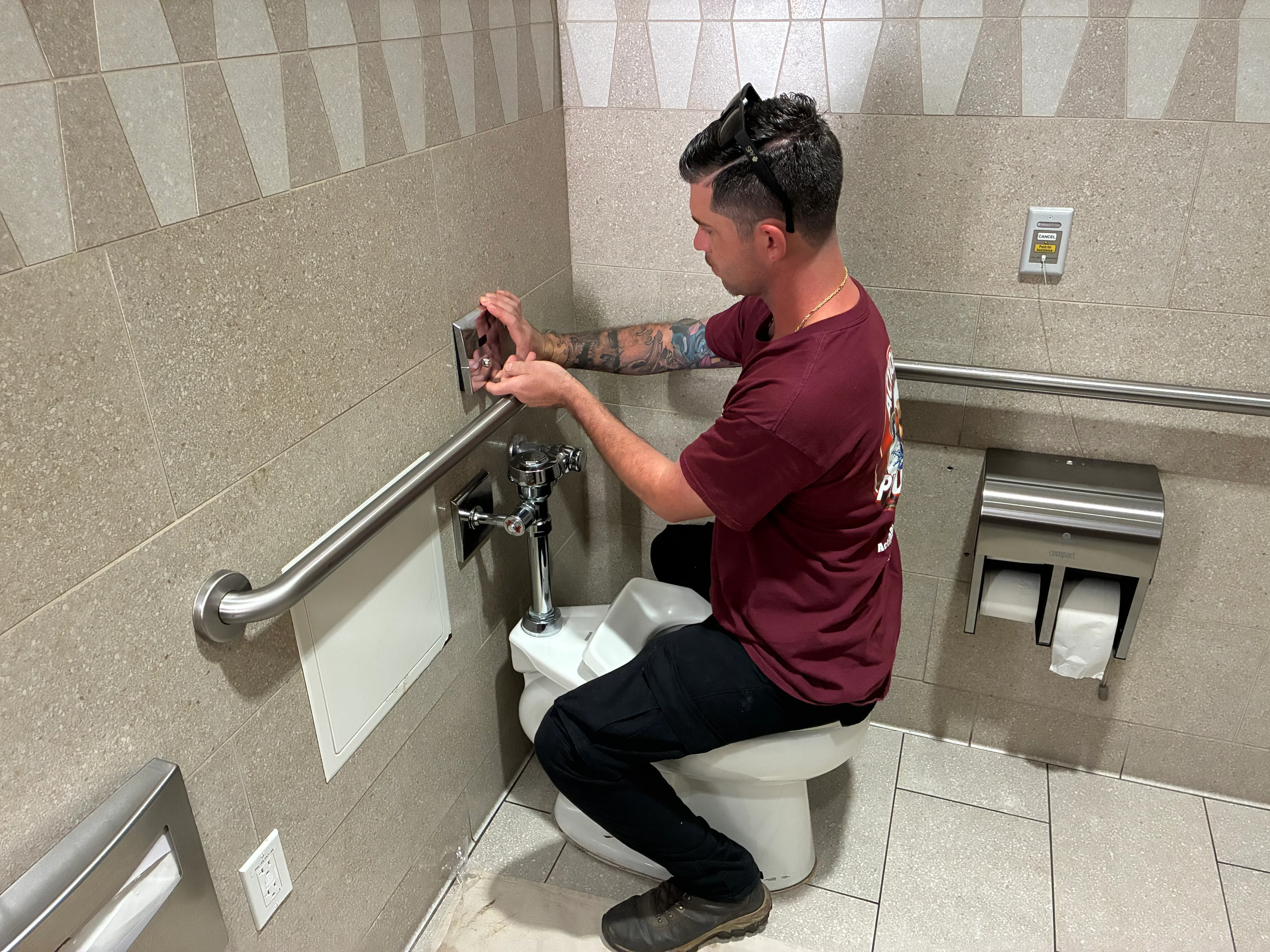 Plumber installing chrome faucet and grab bar on ceramic tile bathroom wall