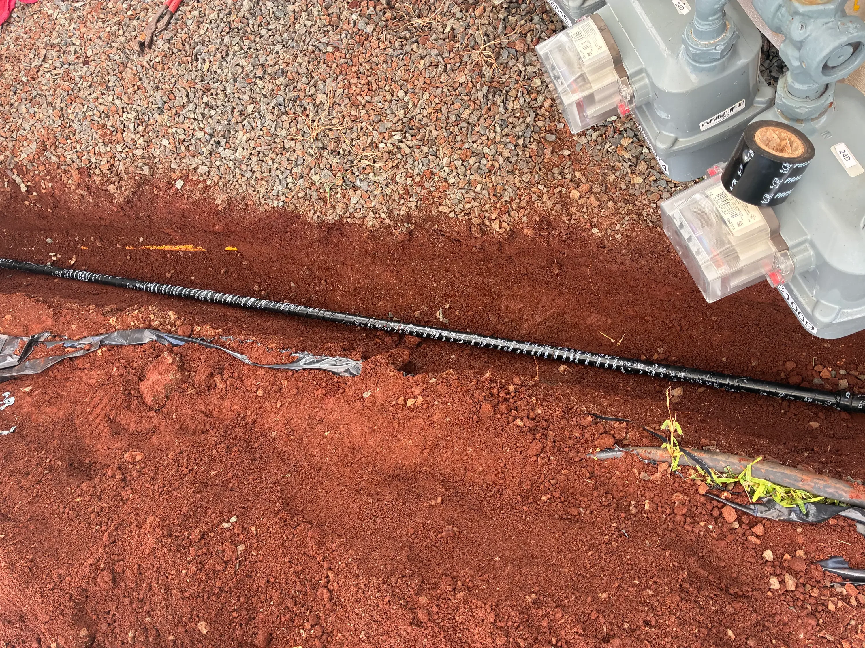 Drip irrigation tubing installed in red soil with gravel mulch and supply components