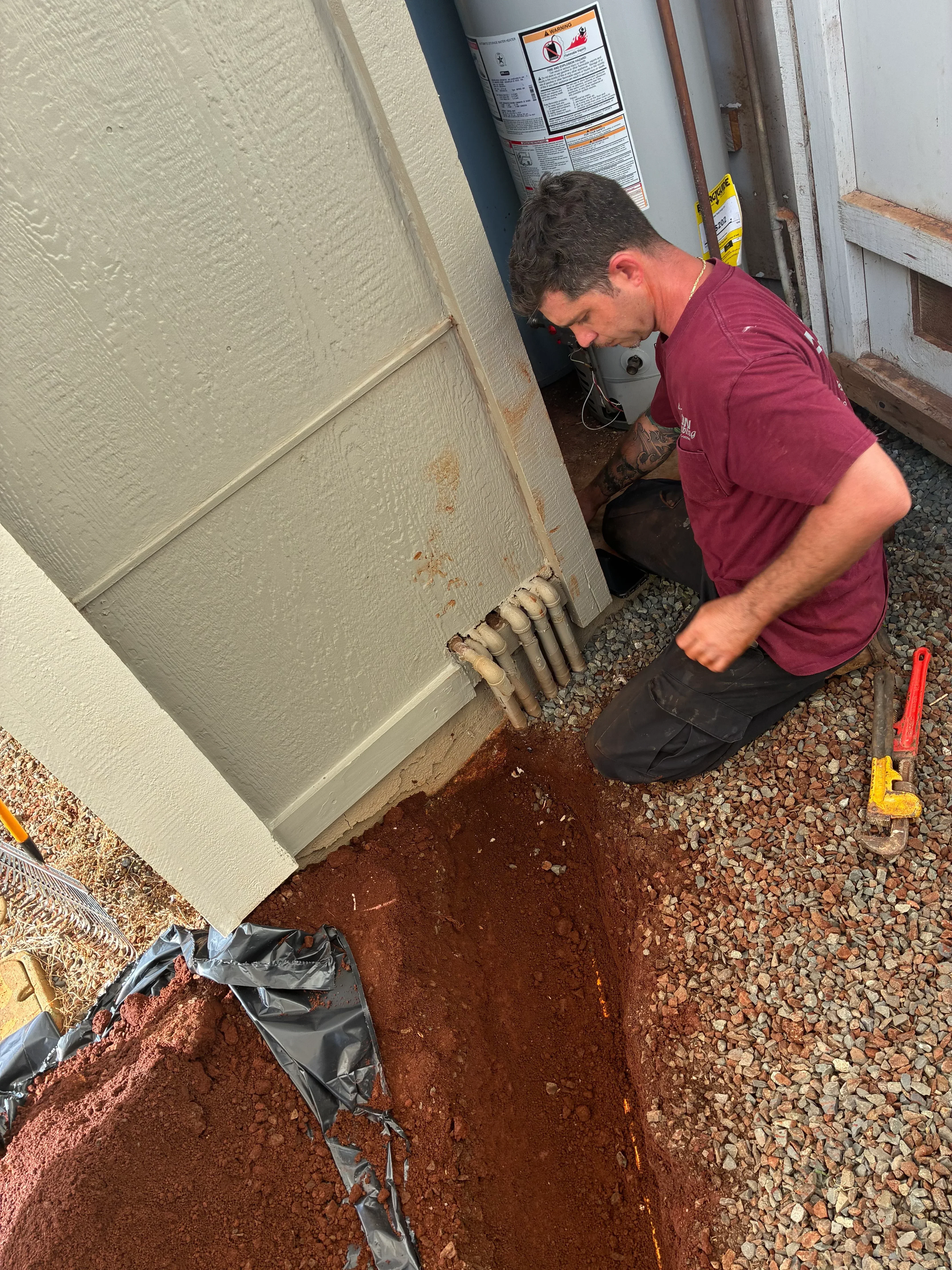 Technician installing perforated drain pipe with gravel bedding along foundation footing