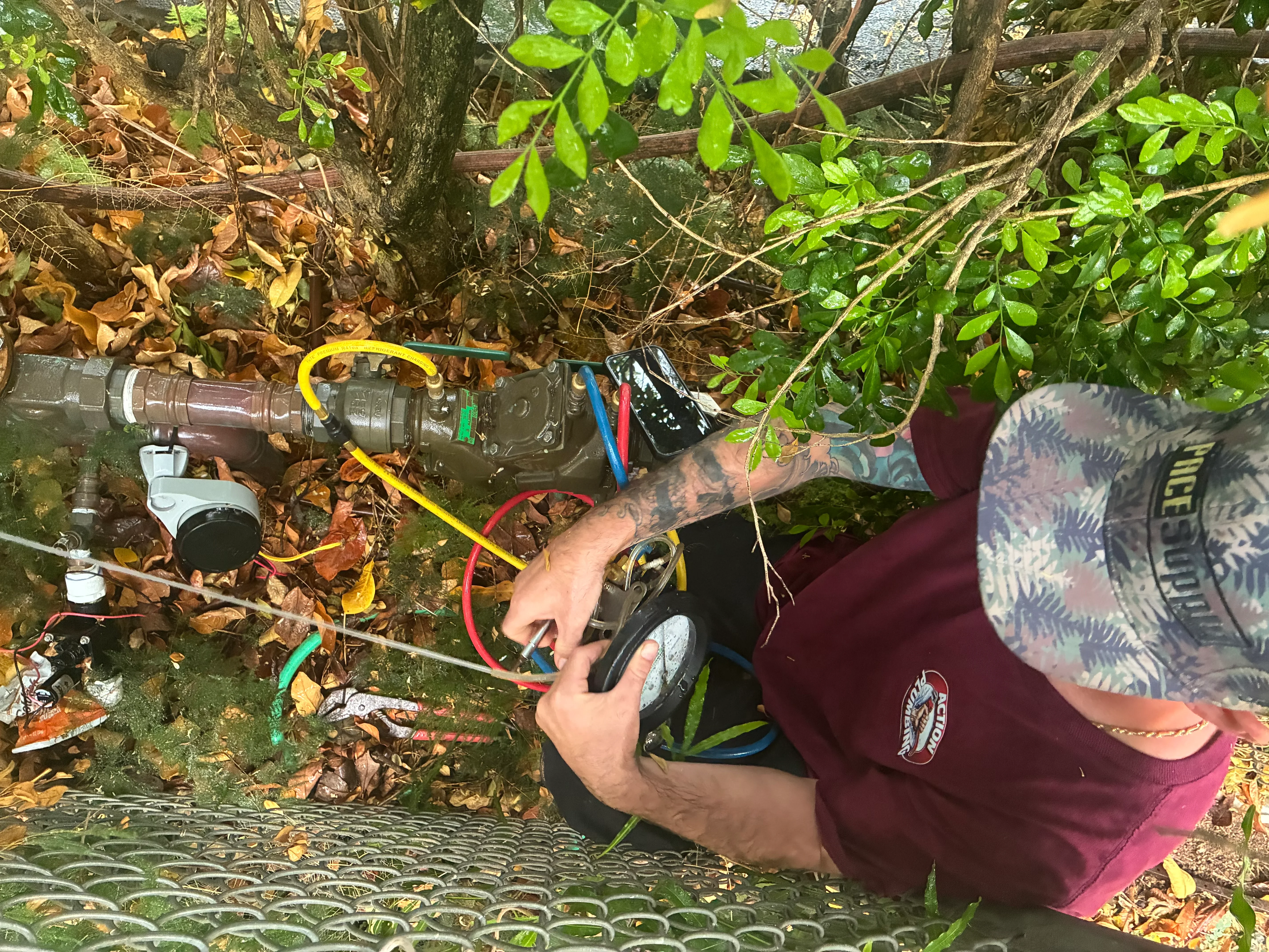 Technician installing brass irrigation valve with color-coded water supply lines in outdoor landscape setting
