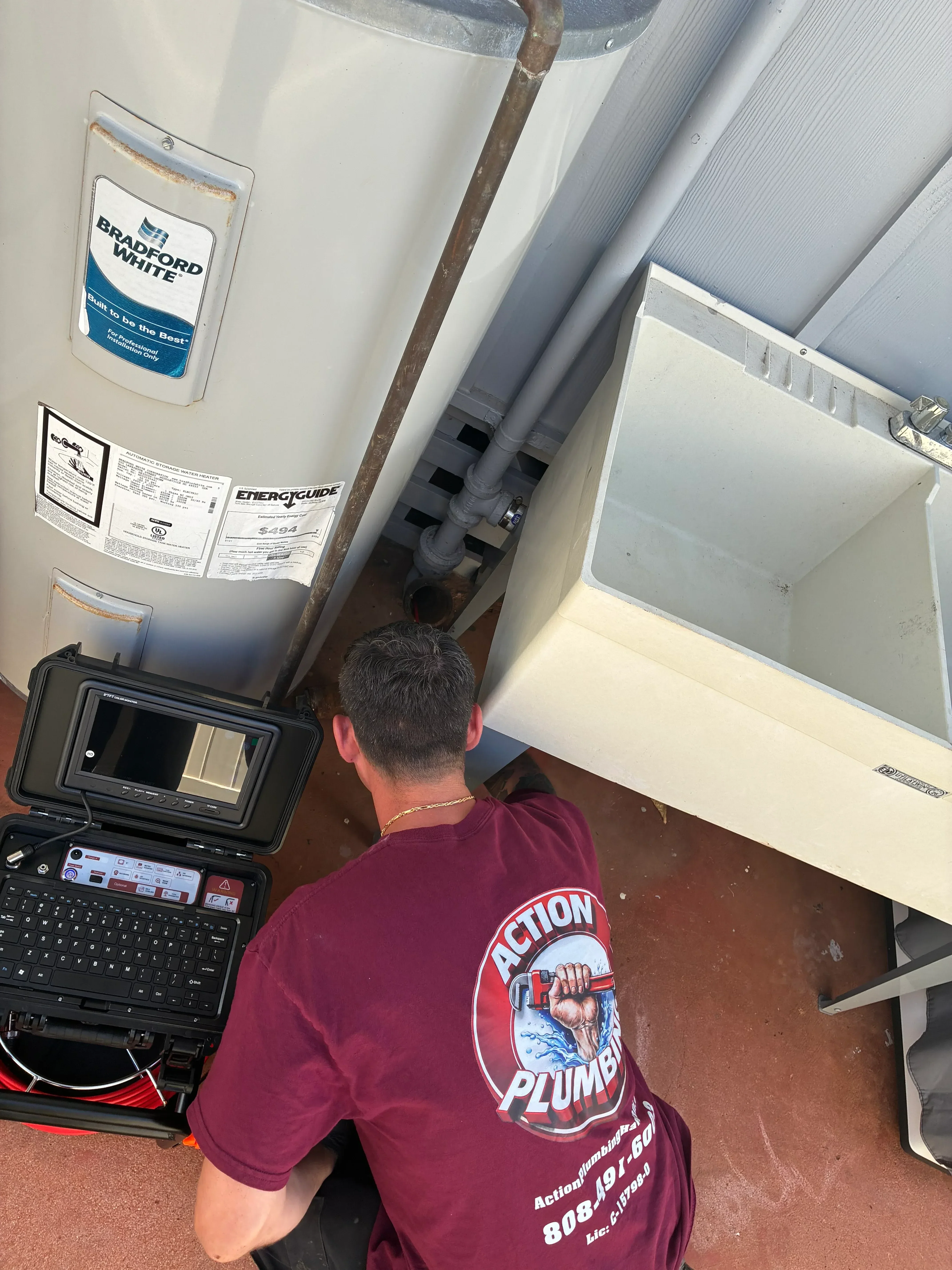 Technician installing white water heater with connected plumbing lines and drain system