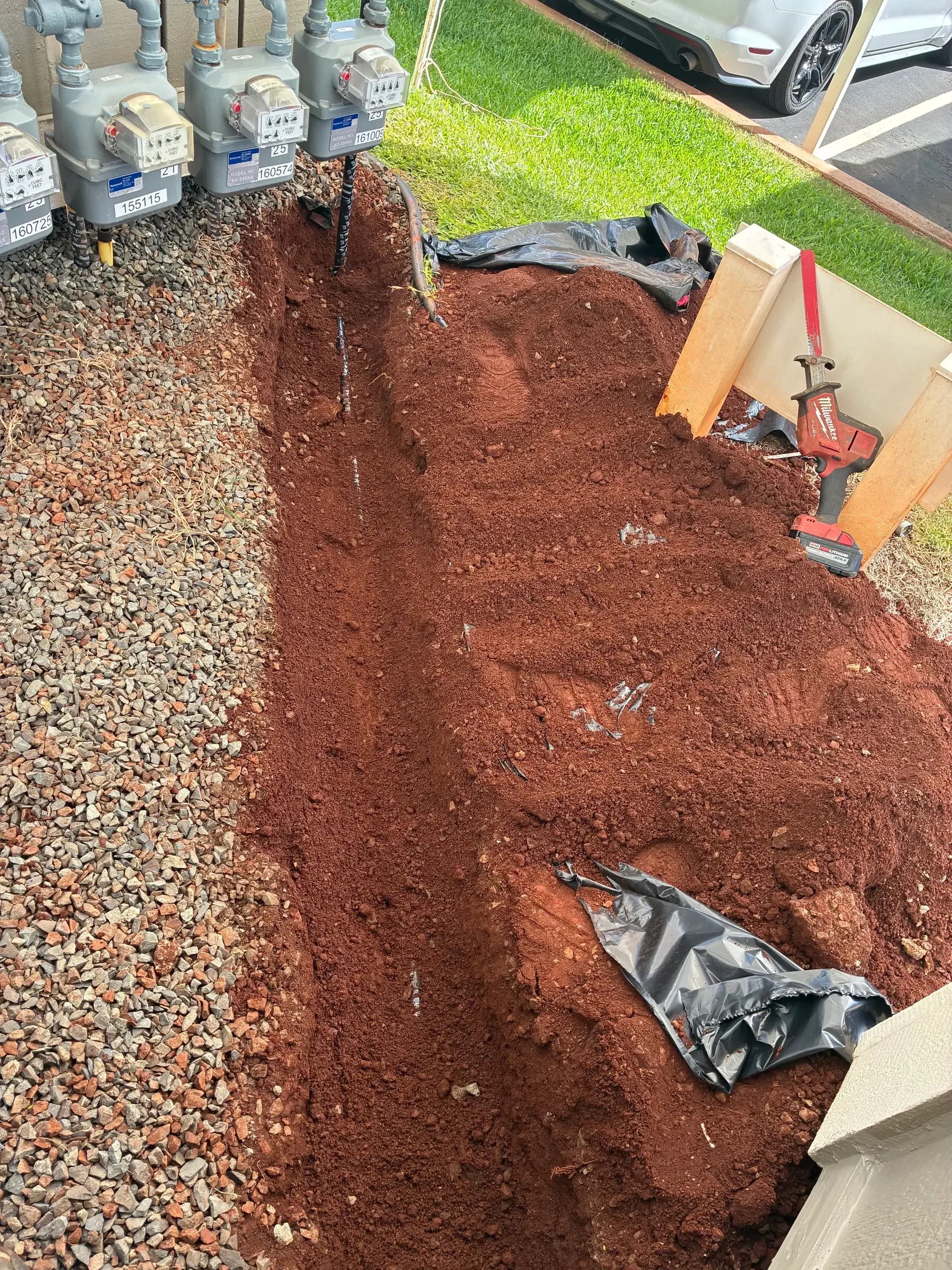 Excavated trench with red clay soil, gravel base, and utility line installation in progress